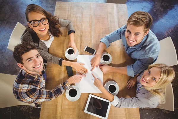 Smiling friends drinking coffee and pointing on paper — Stock Photo, Image