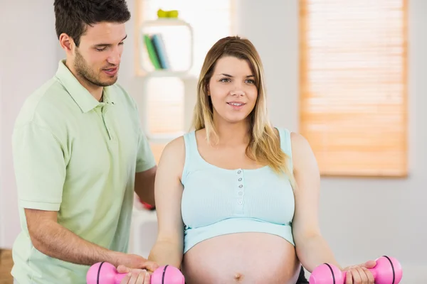 Femme enceinte assise sur une balle d'exercice et soulevant des haltères — Photo