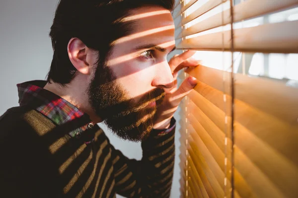 Hipster businessman peeking through blinds — Stock Photo, Image