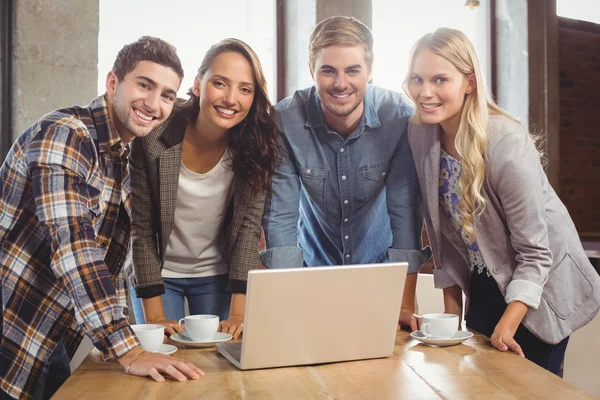 Smiling friends standing around laptop — Stock Photo, Image