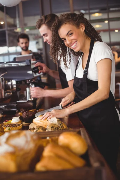 Camarera sonriente cortando pan delante de su colega —  Fotos de Stock