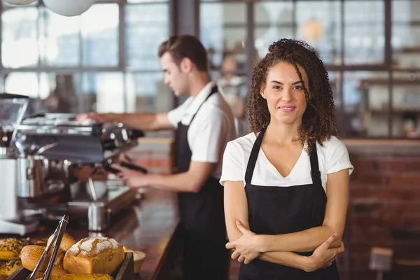 Улыбающаяся официантка со скрещенными руками перед коллегой — стоковое фото