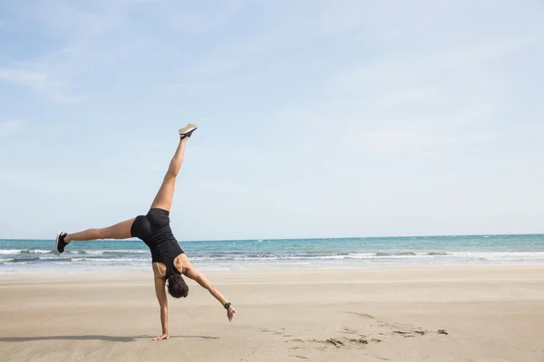 Fit vrouw cartwheeling op het zand — Stockfoto