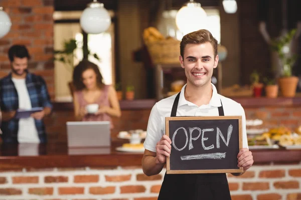 Leende barista anläggning svarta tavlan med öppna tecken — Stockfoto