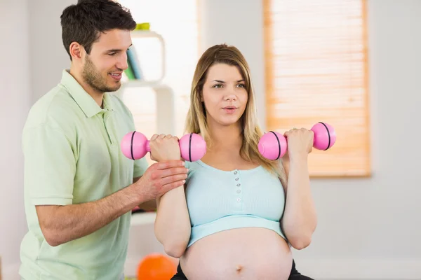 Femme enceinte assise sur une balle d'exercice et soulevant des haltères — Photo