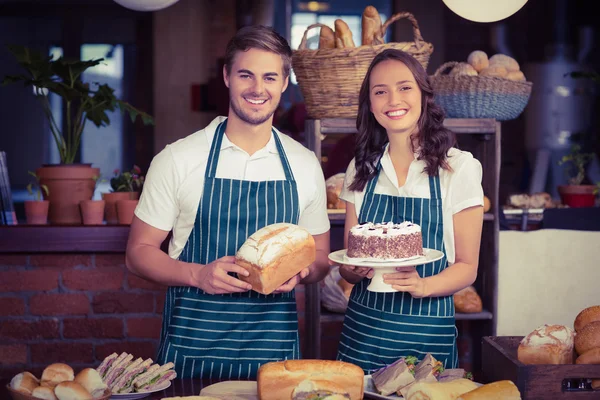 Smiling co-workers showing bread and cake — Stock Photo, Image