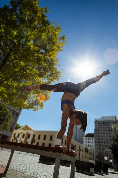 Athletic kvinna utför handstand och gör split på bänk — Stockfoto