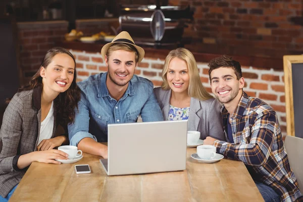 Smiling friends drinking coffee and using laptop — Stock Photo, Image