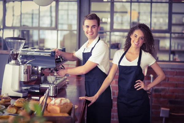 Lächelnde Kellnerin vor einem Kollegen, der Kaffee kocht — Stockfoto