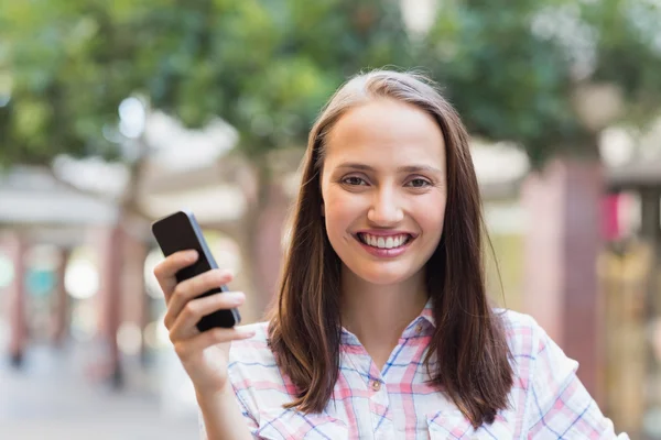 Morena bonita sorrindo para a câmera e segurando um smartphone — Fotografia de Stock