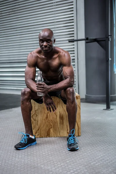 Young Bodybuilder sitting on a wooden Block — Stock Photo, Image