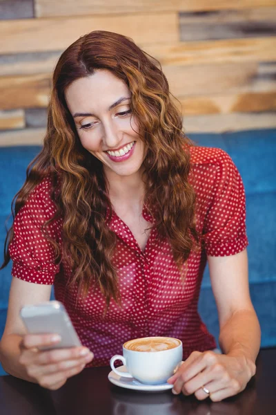 Mujer usando su teléfono móvil y sosteniendo una taza de café — Foto de Stock