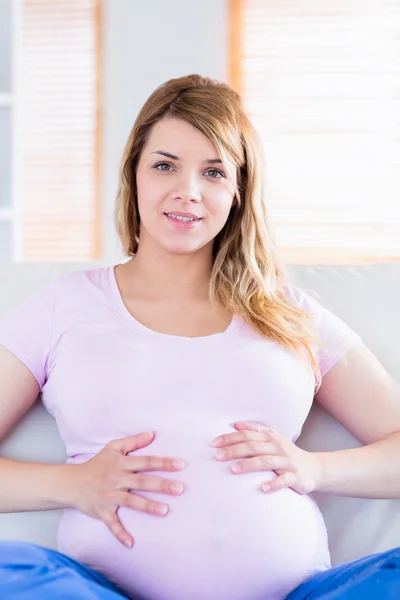 怀孕的女人看着相机用手在肚子上 — 图库照片