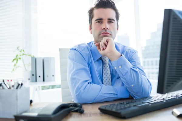 Businessman sitting on an office chair with hand on chin — Stock Photo, Image