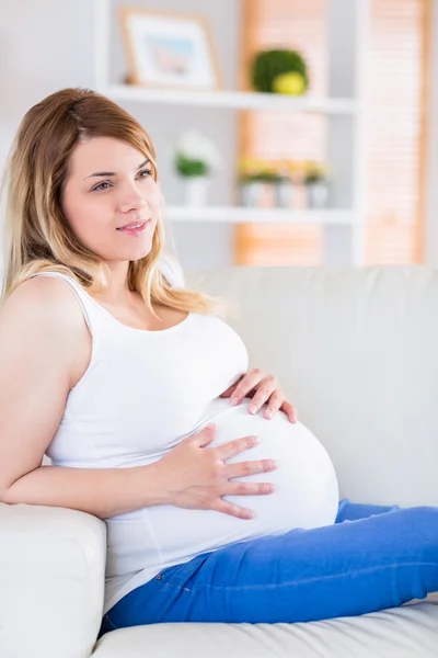 Zwangere vrouw aanraken haar buik op de Bank — Stockfoto