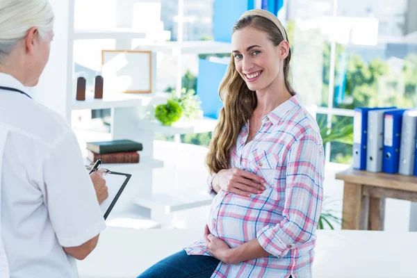 Έγκυος γυναίκα χαμογελώντας σε φωτογραφική μηχανή σε ένα τραπέζι εξέταση — Φωτογραφία Αρχείου