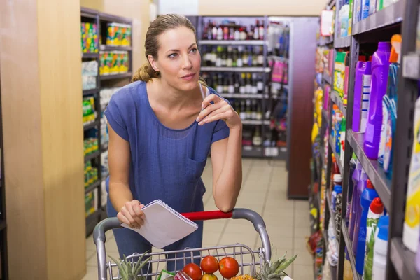 Mooie vrouw kijken naar product op de plank en houden kruidenier lis — Stockfoto