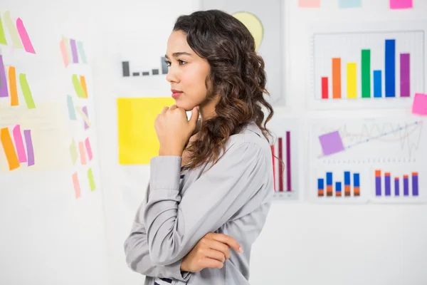Young thinking businesswoman looking at sticky notes — Stock Photo, Image