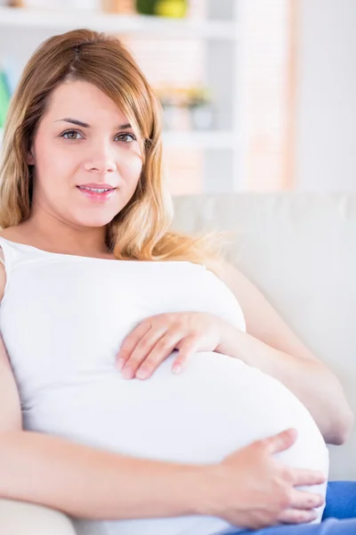 Беременная женщина смотрит в камеру на диване — стоковое фото