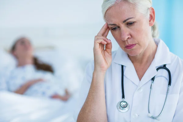 Preoccupato medico femminile guardando lontano mentre il suo paziente a riposo — Foto Stock