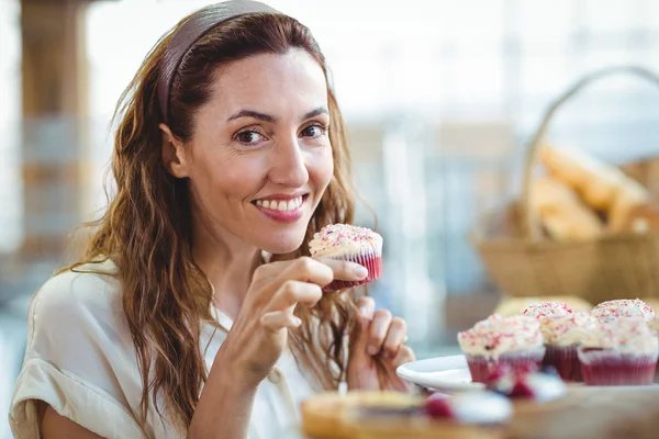 Pretty brunette looking at camera and holding cupcake — Stock Photo, Image
