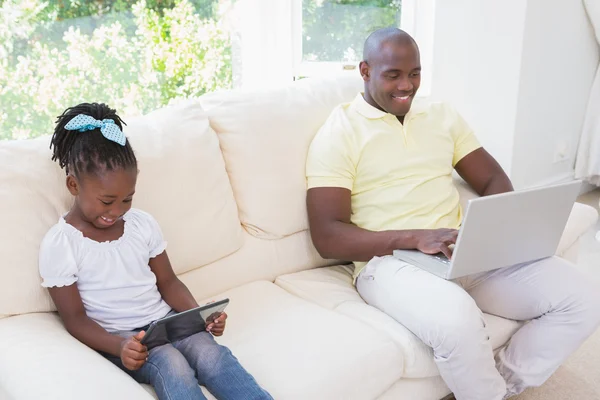 Feliz padre sonriente usando el portátil y su hija usando la tableta — Foto de Stock