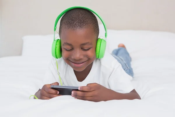 Niño usando smartphone y escuchando música en la cama — Foto de Stock