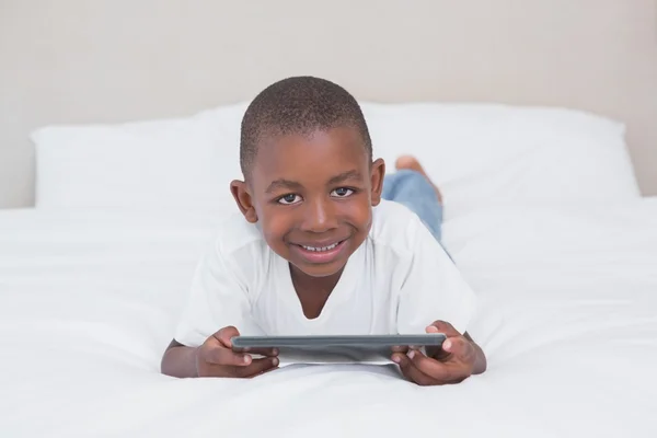 Retrato de un niño bonito usando tableta digital en la cama —  Fotos de Stock