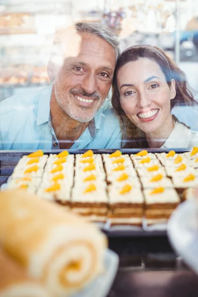 Pareja feliz mirando pasteles a través del vidrio — Foto de Stock