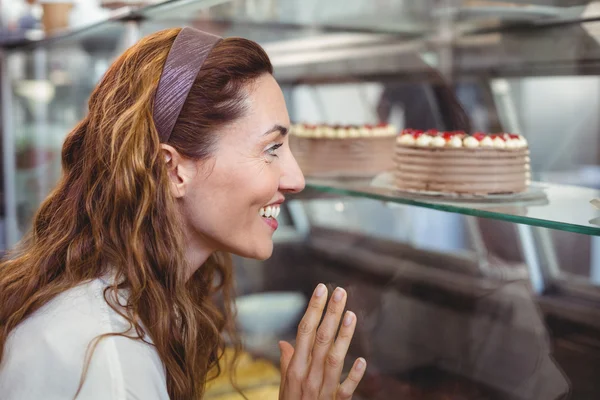 Bella bruna guardando le torte attraverso il vetro — Foto Stock