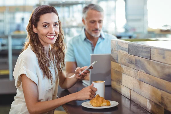 Söt brunett ler mot kameran och använda sin smartphone — Stockfoto