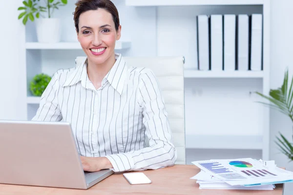 Brunette smiling businesswoman using laptop — Stock Photo, Image