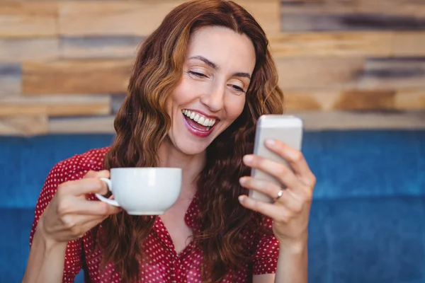 Mujer usando su teléfono móvil y sosteniendo una taza de café — Foto de Stock