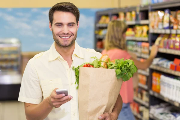 Retrato de un hombre guapo sonriente comprando productos alimenticios y usando —  Fotos de Stock