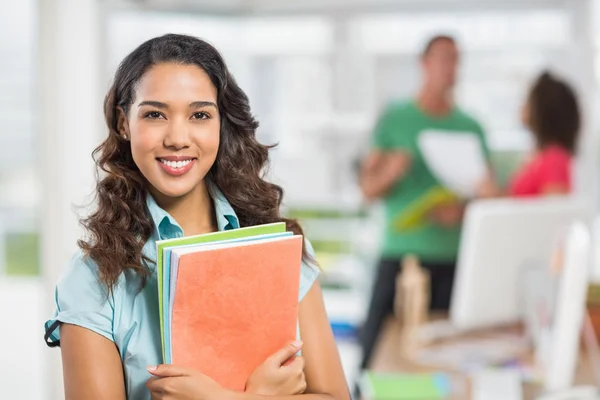 Mujer de negocios sosteniendo archivos con sus colegas detrás de ella —  Fotos de Stock