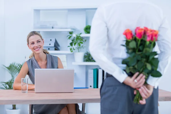 Businessman hiding flowers behind back for colleague