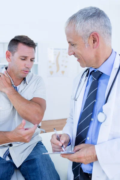 Doctor examining his patient and writing on clipboard — Stock Photo, Image