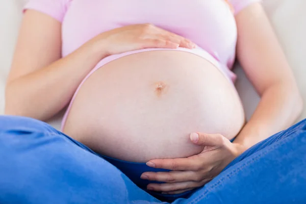 Närbild på gravid kvinna sitter på soffan röra hennes mage — Stockfoto