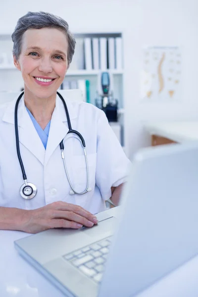 Happy doctor looking at camera and using her smartphone — Stock Photo, Image