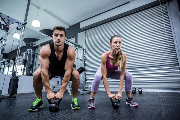 Un couple musclé soulevant kettlebells — Photo