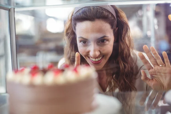 Bonita morena mirando pastel de chocolate a través del vaso — Foto de Stock
