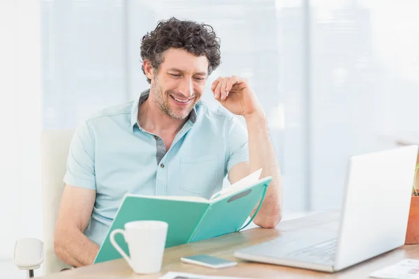 Lächelnder Gelegenheitsunternehmer mit Büchern am Schreibtisch — Stockfoto