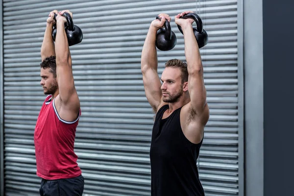 Muscular men lifting a kettle bell — Stock Photo, Image