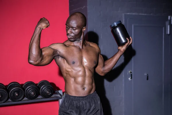 Young Bodybuilder looking at his muscles while holding a bottle — Stock Photo, Image