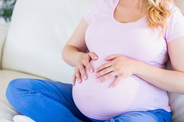 Femme enceinte assise sur le canapé touchant son ventre — Photo