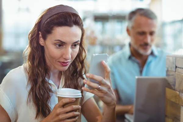 Morena bonita usando seu smartphone com café na mão — Fotografia de Stock