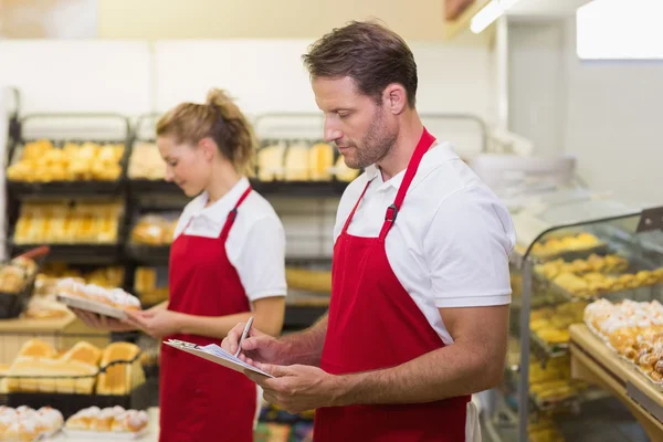 Zijaanzicht van twee bakkers schrijven op een notitieblok — Stockfoto