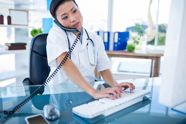 Médico ter telefonema e usando seu computador — Fotografia de Stock