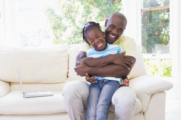 Счастливый улыбающийся отец обнимается с дочерью на диване — стоковое фото