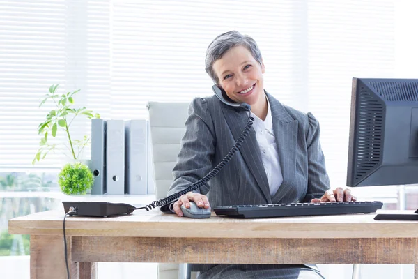 Smiling portrait businesswoman phoning and using computer — Stock Photo, Image